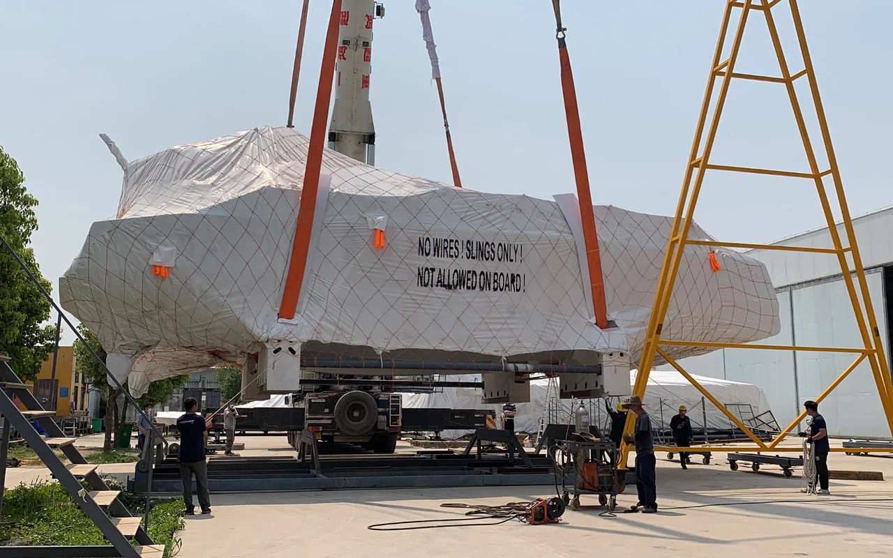A shrink-wrapped Cure catamaran being craned onto a transporter for shipping